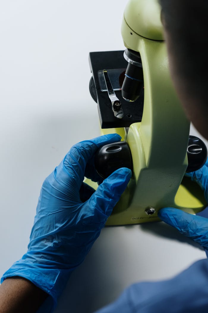 Close-up of a scientist adjusting a microscope with gloved hands in a laboratory.