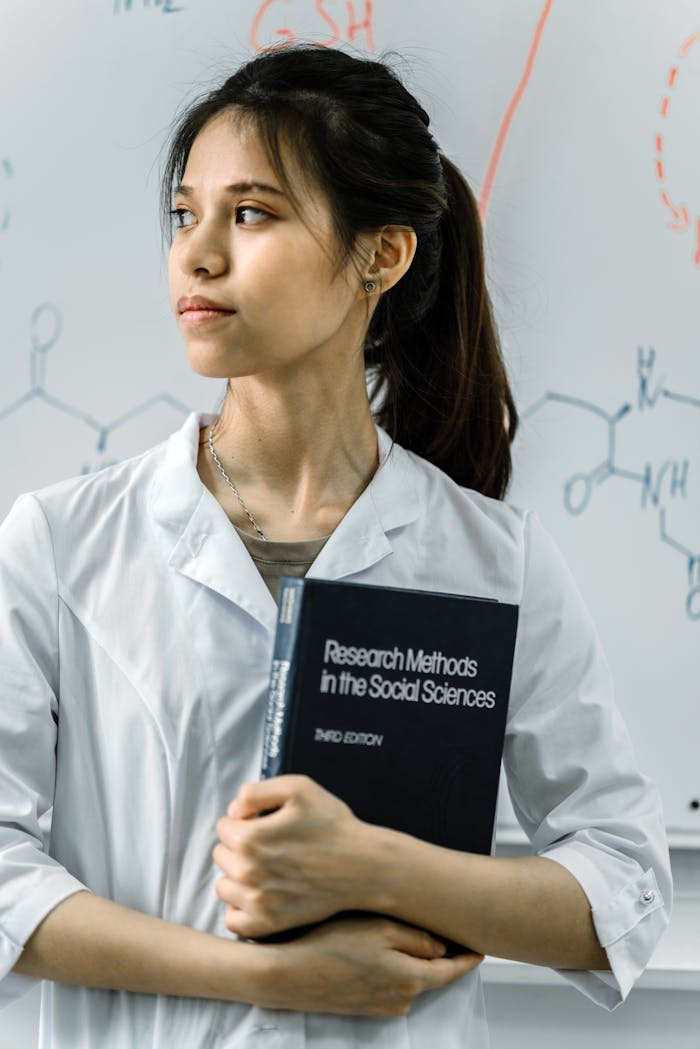 Portrait of young female scientist holding a book in a lab setting with a formula background.