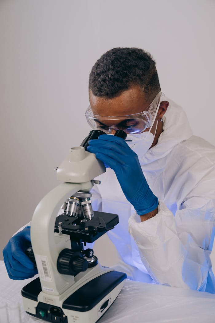 A focused scientist in protective gear conducting research using a microscope in a laboratory.